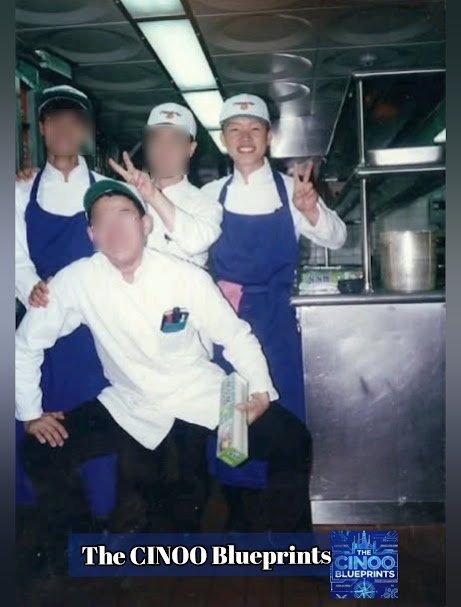 Four professional kitchen staff members posing inside the Millennium Hilton Hotel buffet restaurant kitchen, with the author CINOO standing at the far right end smiling alongside coworkers in aprons and chef uniforms.